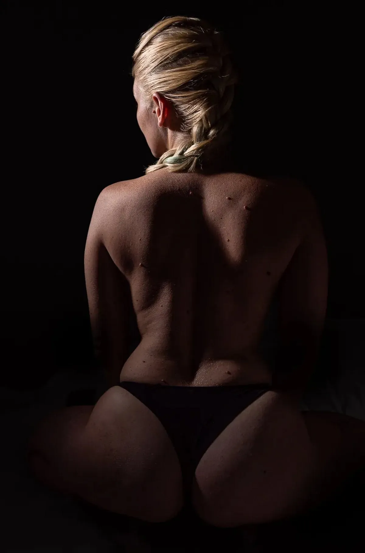 Back-view artistic nude portrait of a seated woman shaped by warm directional light