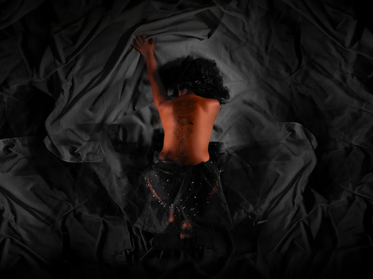 Overhead artistic nude portrait of a woman lying on dark bedding with controlled framing