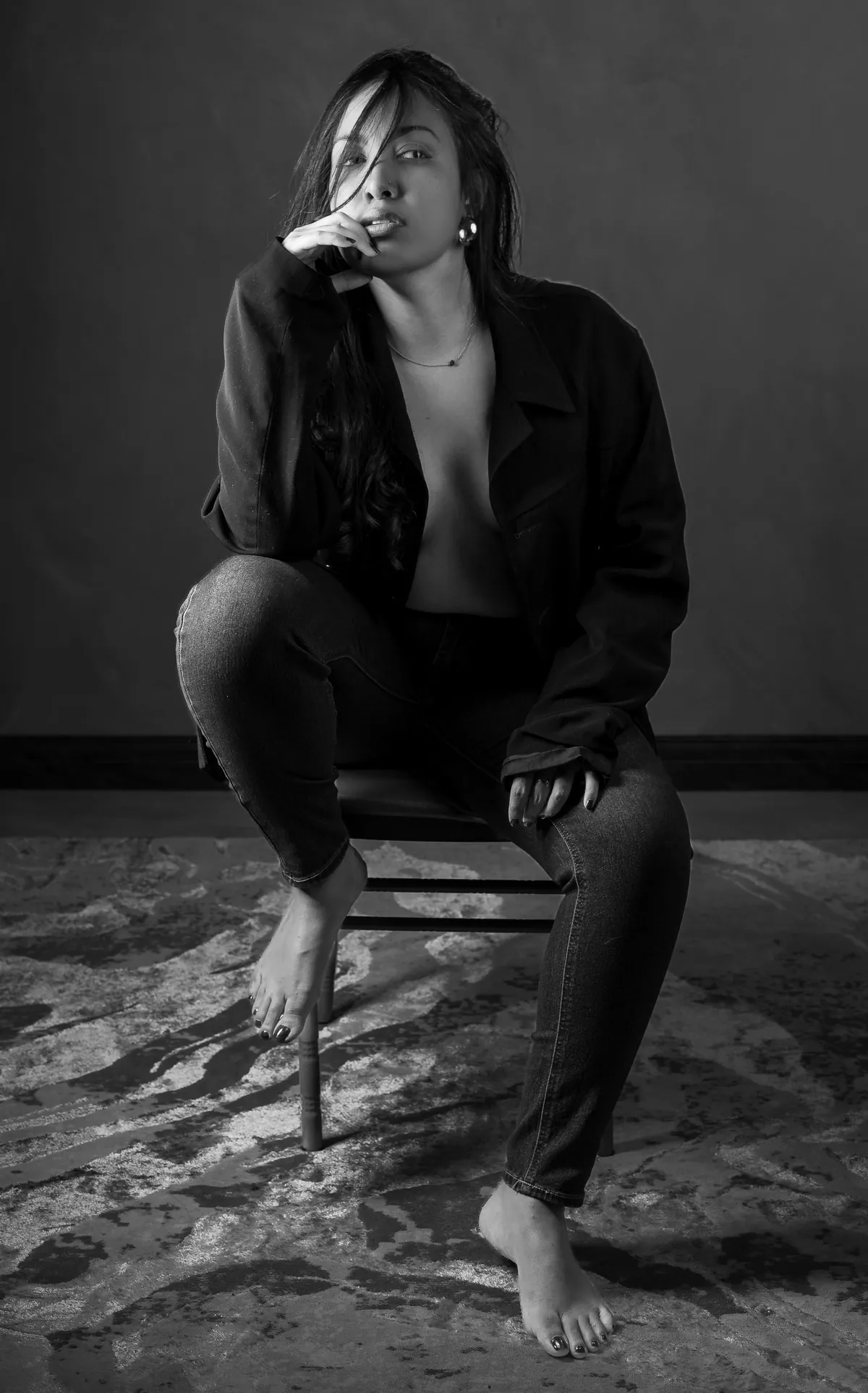 Artistic semi-nude portrait of a woman seated forward on a chair under soft studio light