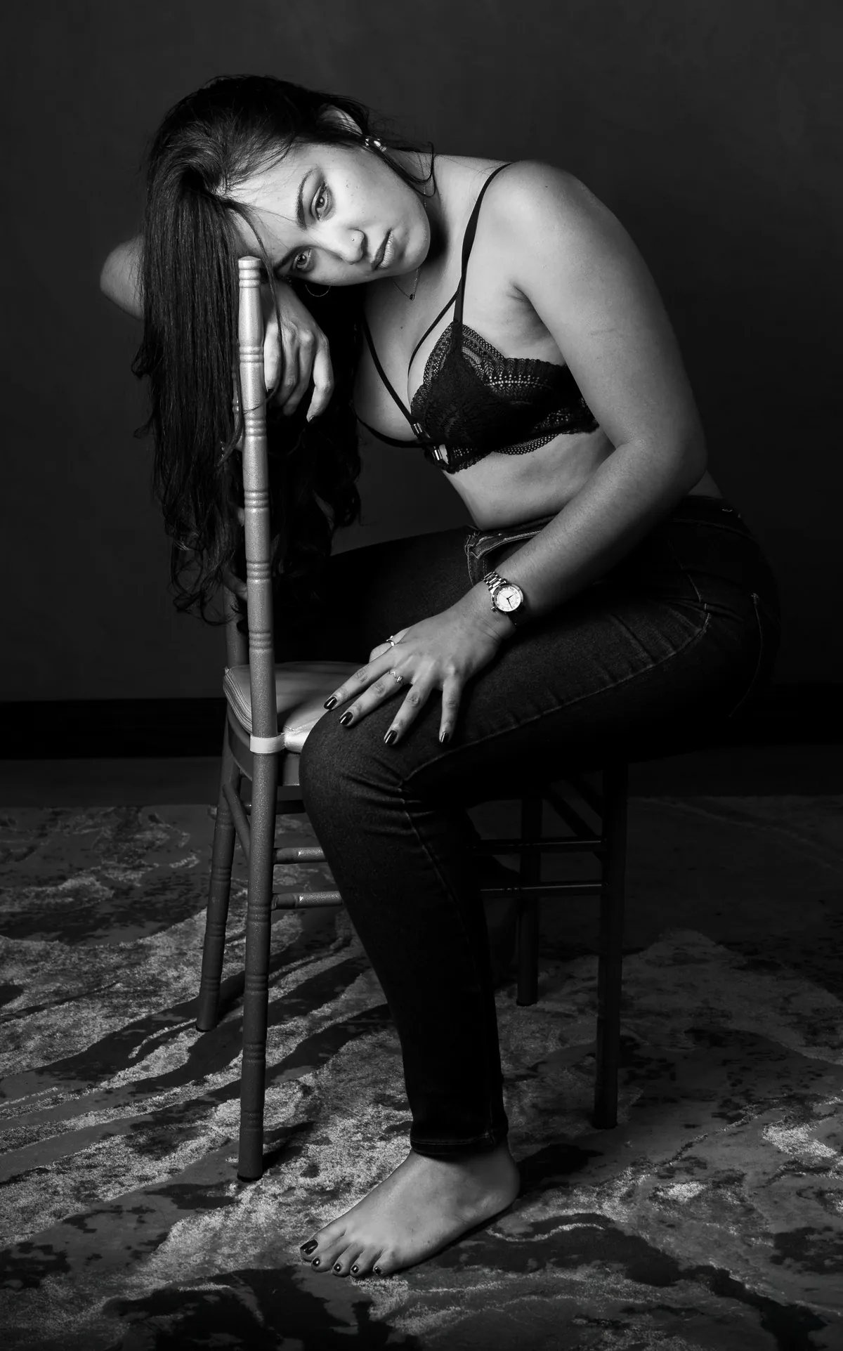 Low-key semi-nude portrait of a woman seated on a chair with expressive posture