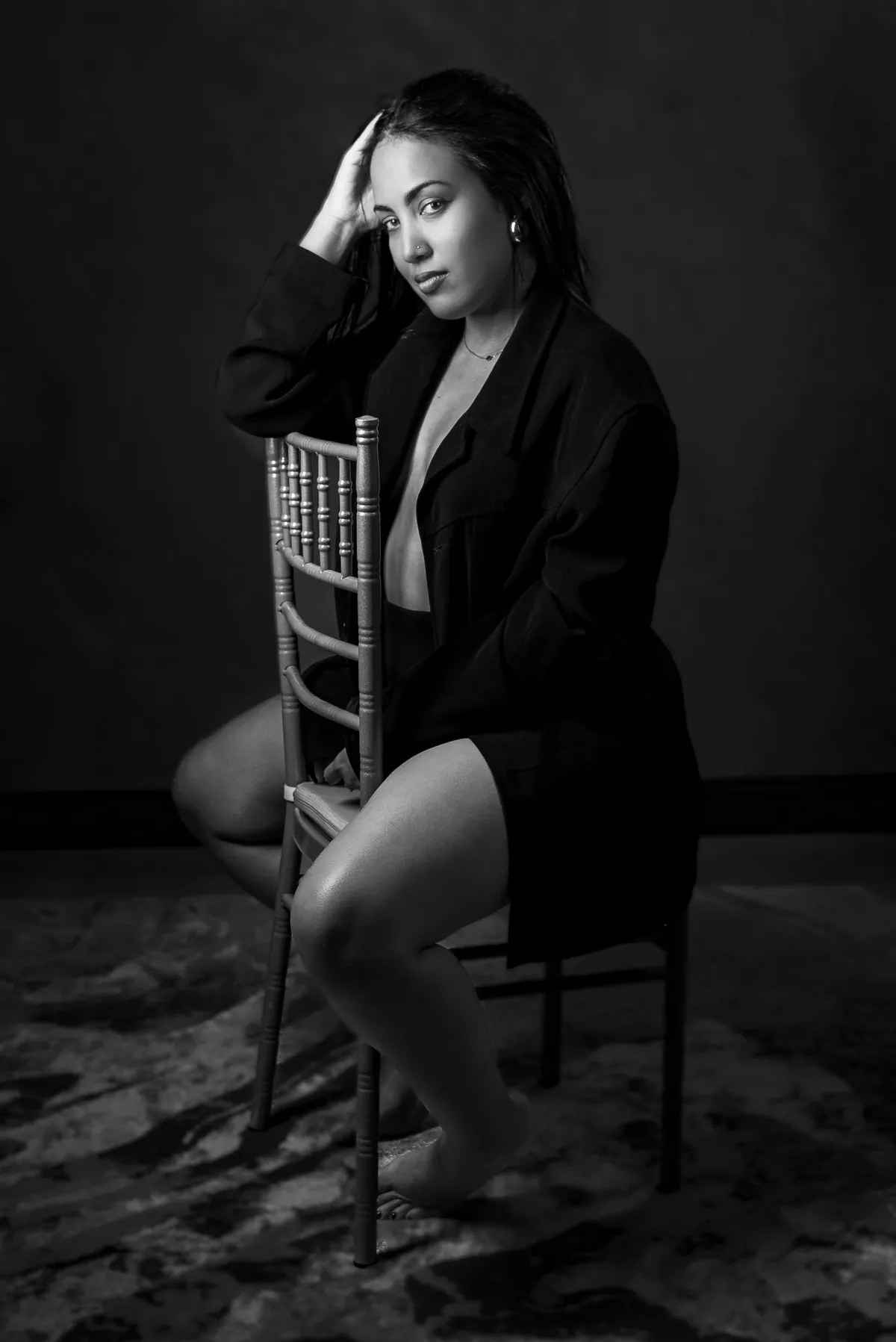 Black-and-white seated portrait of a woman wearing an open shirt in a private studio setting