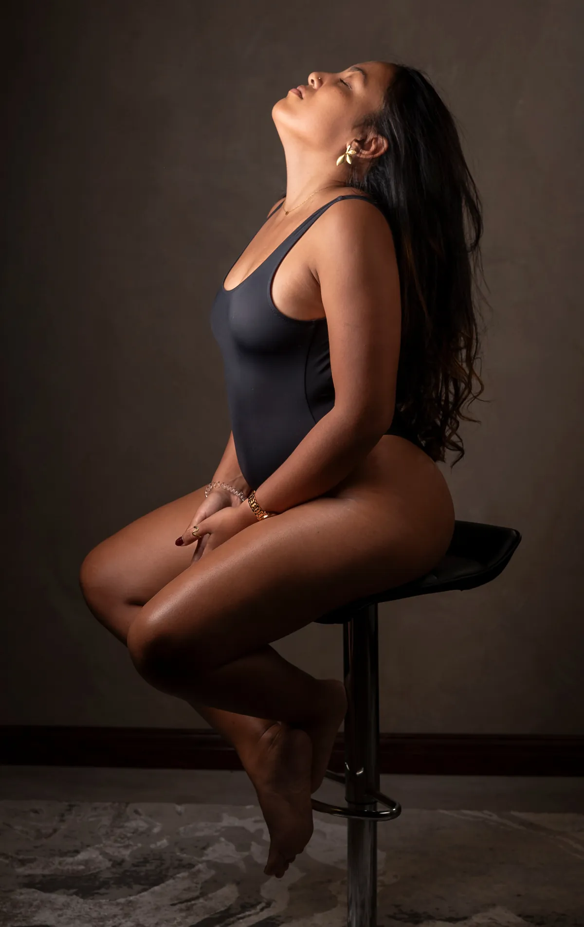 Seated semi-nude studio portrait of a woman posing confidently on a stool