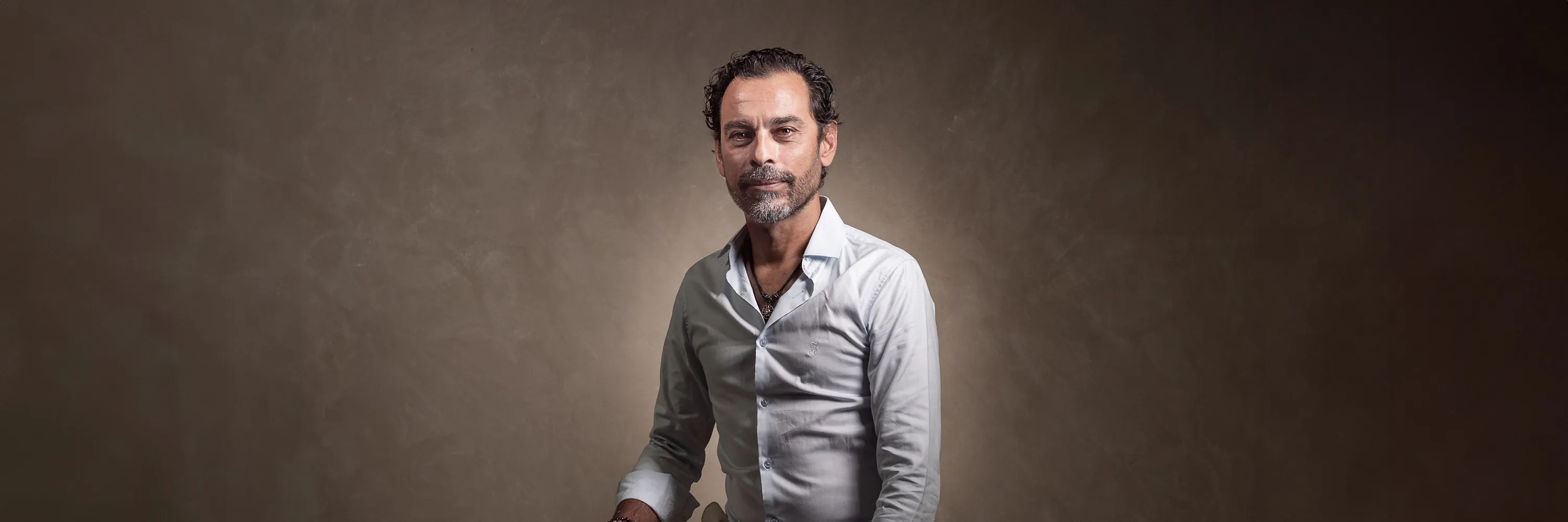Professional studio portrait of a seated man against a warm neutral background