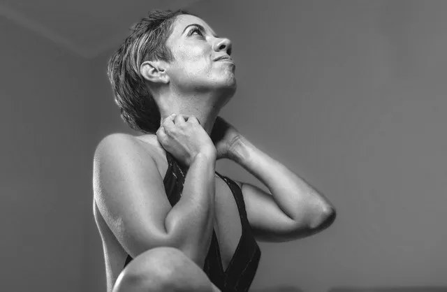 Mauritian woman in black dress sitting cross-legged on bed during studio photoshoot