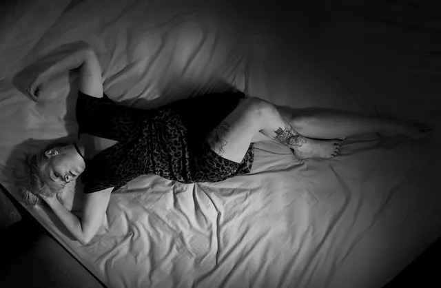 Black and white boudoir photo of tattooed model lying on white sheets