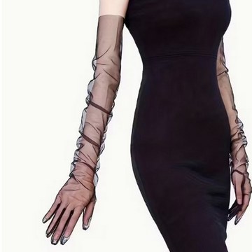Woman wearing long sheer black mesh gloves with a fitted black dress during a studio photoshoot.